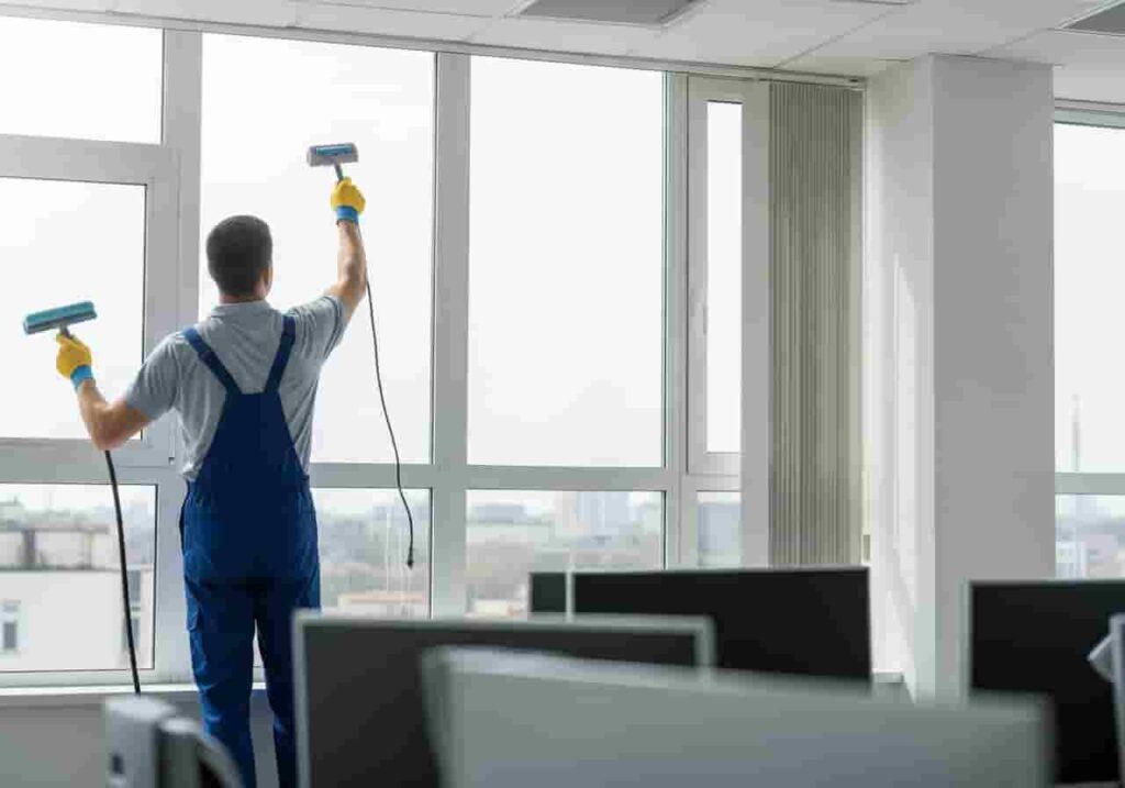 Candidato limpiando vidrios en edificio moderno con arnés de seguridad.